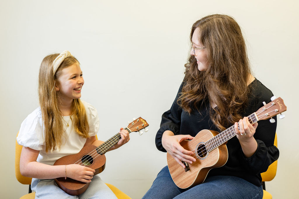 Student and teacher smiling while playing ukulele together during music lessons in Oklahoma City.